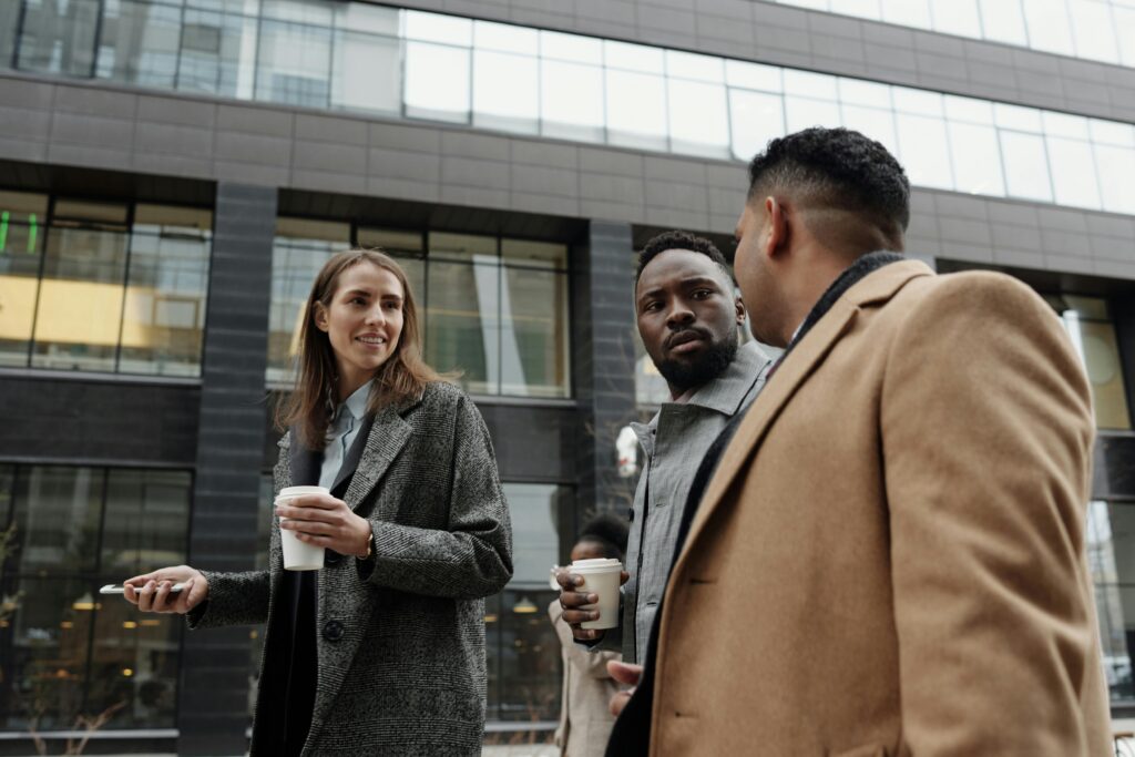 Three coworkers walk and talk outside a contemporary office building, reflecting the kind of supportive, engaging work culture fostered by strong employee health plans.