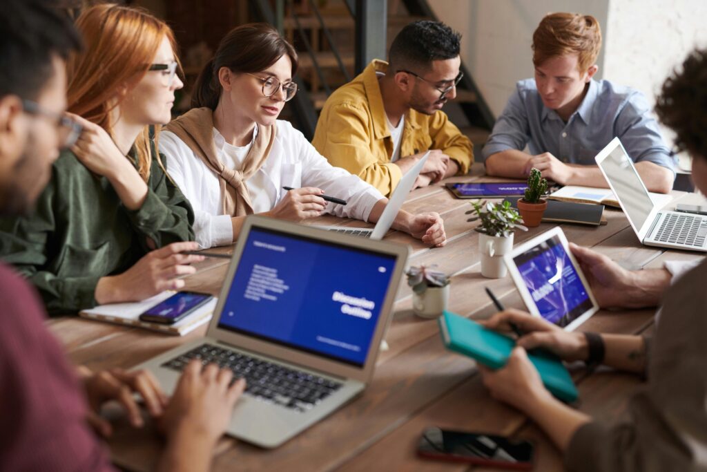 A diverse group of professionals collaborates around a shared table with laptops and digital devices, symbolizing the productivity and inclusion enabled by comprehensive employee health plans.