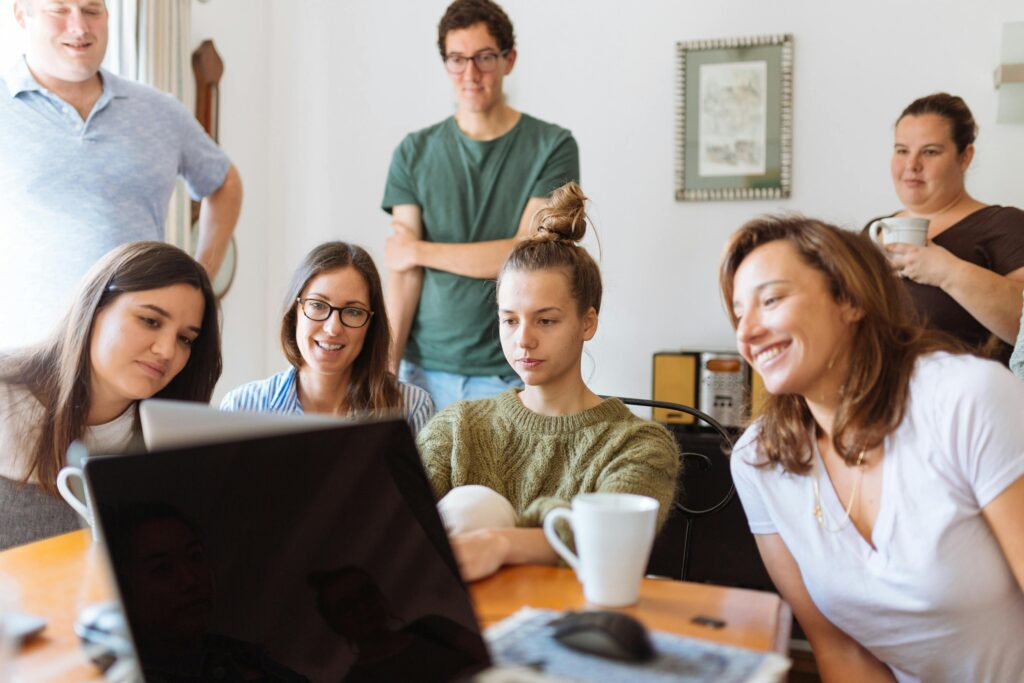 A group of coworkers gathered around a laptop, smiling and engaging in a casual workspace, reflecting the sense of community supported by California insurance plans.