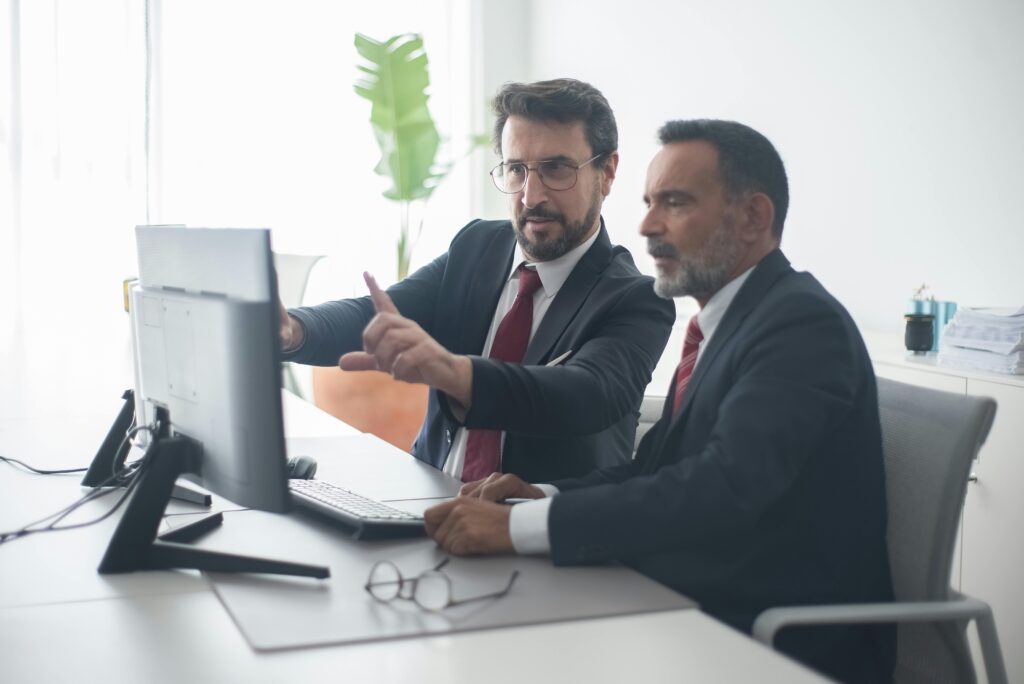 Two business professionals in suits analyzing information on a computer monitor, illustrating the strategic importance of choosing the right California insurance plans for executive and managerial teams.