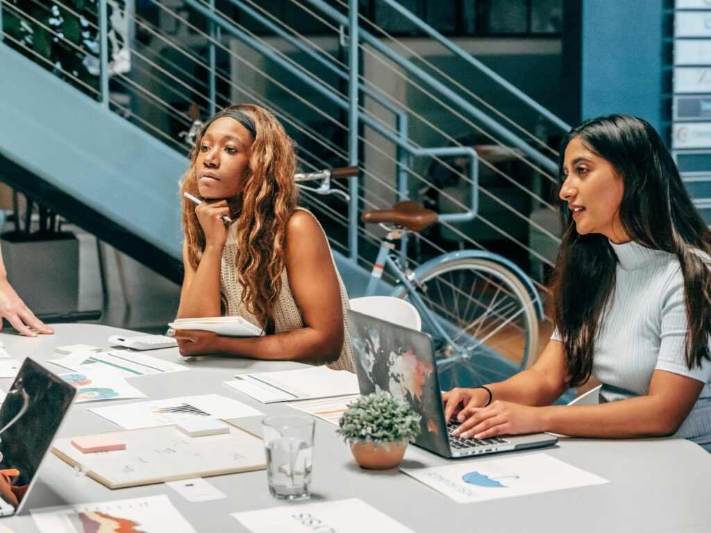 Two women in a creative office environment discussing business strategy, showcasing how California insurance plans can enhance workplace confidence and well-being.
