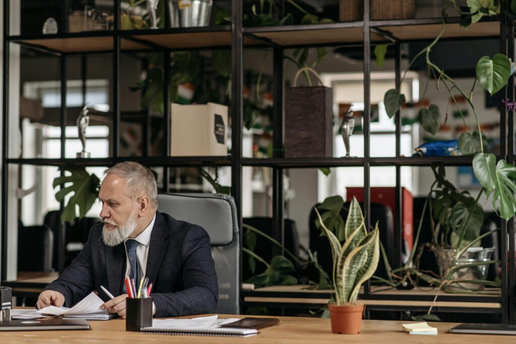 A senior executive reviews paperwork at his desk in a modern, plant-filled office, symbolizing thoughtful planning and the stability offered by comprehensive California insurance plans.