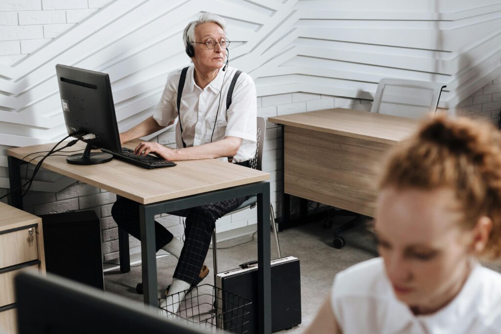 An older professional using a desktop computer with a headset in a modern office, highlighting how California insurance plans can provide essential support for workers of all ages in evolving job roles.