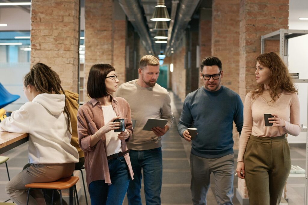 Group of coworkers walking through an industrial-style office hallway while discussing work, symbolizing team collaboration and accessibility of California insurance plans.