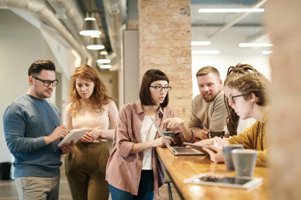 Coworkers gathered around a communal workspace, reviewing documents and laptops, representing open dialogue and employee participation in choosing California insurance plans.