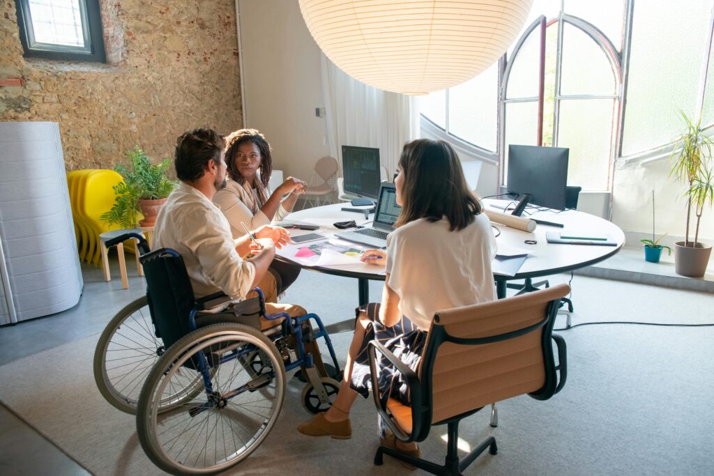 Inclusive workplace meeting with a team discussing employee health plans, featuring a man in a wheelchair actively engaged in the conversation.