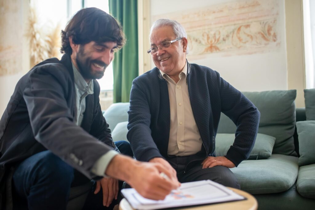 Two men sitting in a relaxed setting, smiling while reviewing documents together, symbolizing the personalized support and peace of mind offered by comprehensive employee health plans.