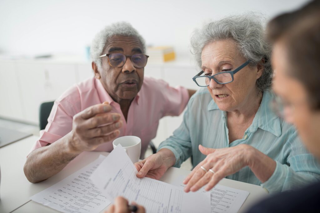 An elderly couple reviews paperwork with a consultant, discussing the details of California insurance plans together.