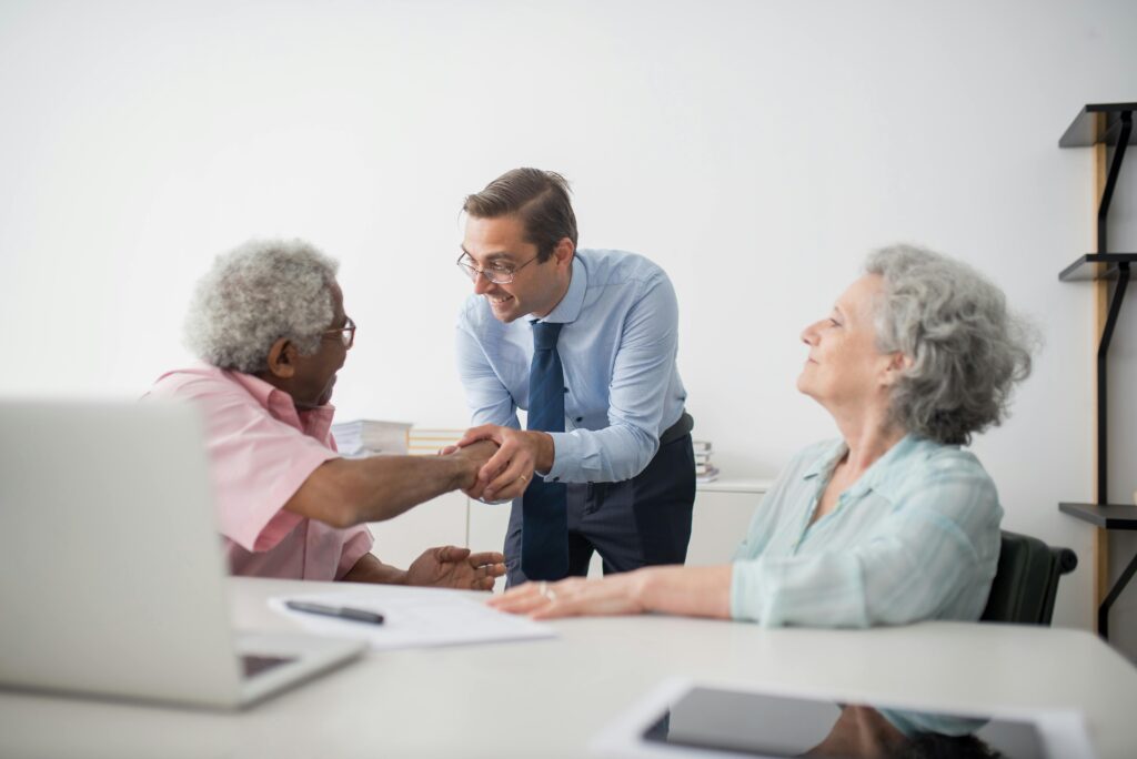 A financial advisor shakes hands with an elderly client, finalizing paperwork related to California insurance plans.