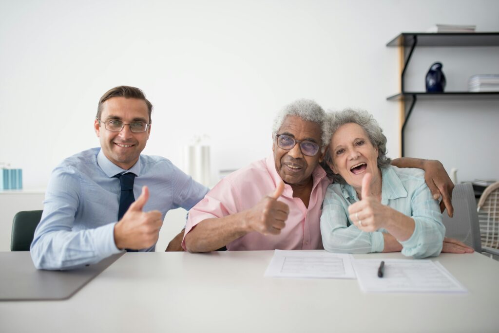 A happy elderly couple poses with their insurance advisor, all smiling and giving a thumbs up after selecting California insurance plans.