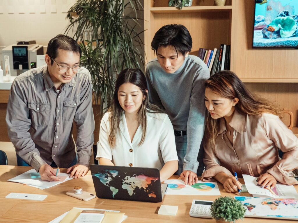 A focused team collaborating around a laptop with world map graphics, reviewing charts and documents related to employee health plans.
