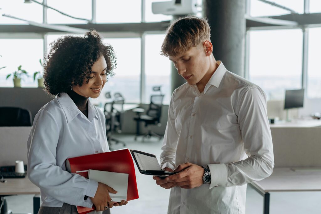Two professionals review employee health plans on a digital device in a bright office setting.