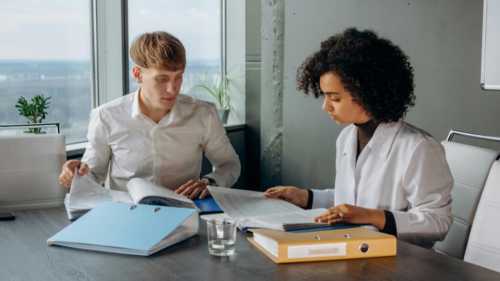 A young man and woman analyze documents related to employee health plans in a boardroom.