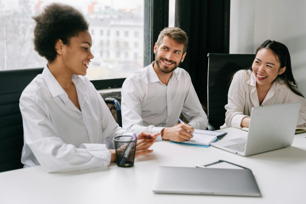 Three coworkers having a cheerful discussion at the office while reviewing a laptop, representing collaboration when evaluating California insurance plans.