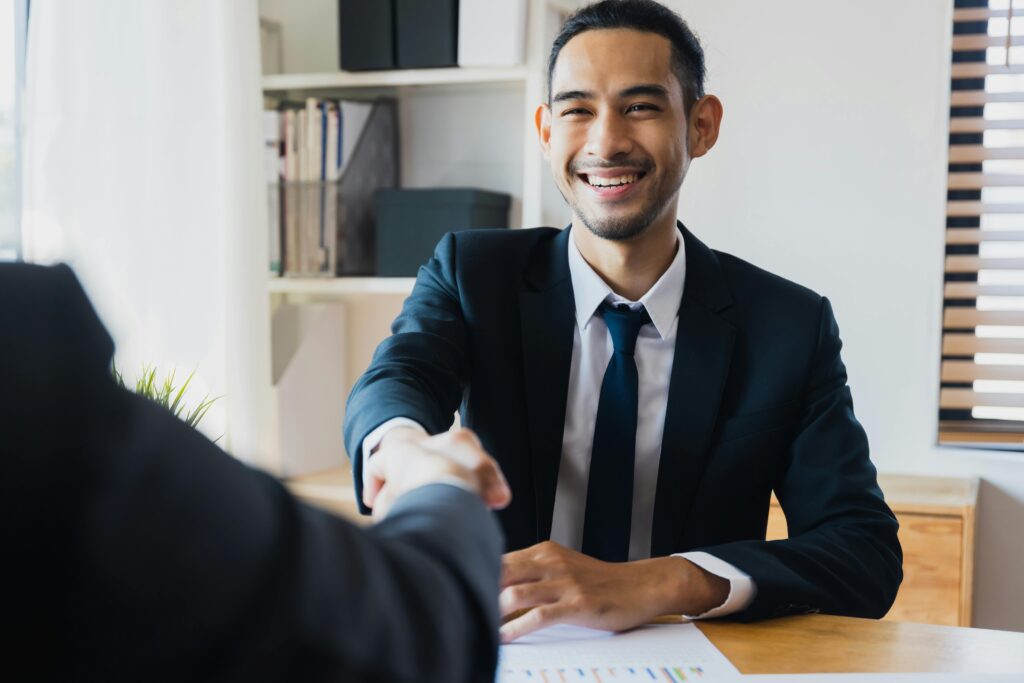 A professional in a suit smiles while shaking hands across a desk, finalizing a partnership related to ACA California compliance for employee benefits.