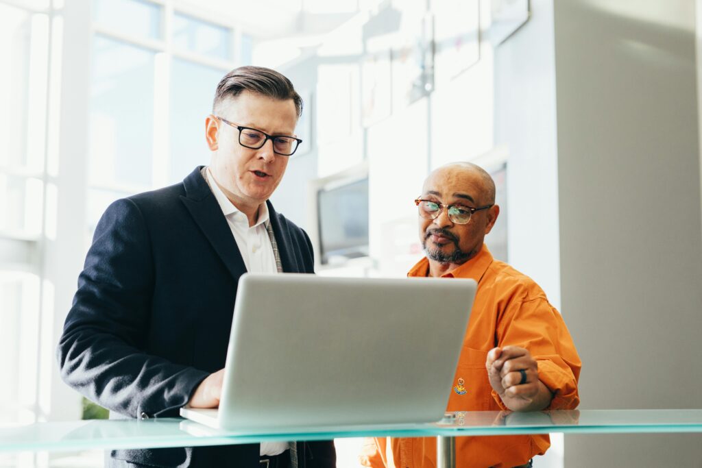 Businessmen in discussion while reviewing California insurance plans on a laptop in a brightly lit office lobby.