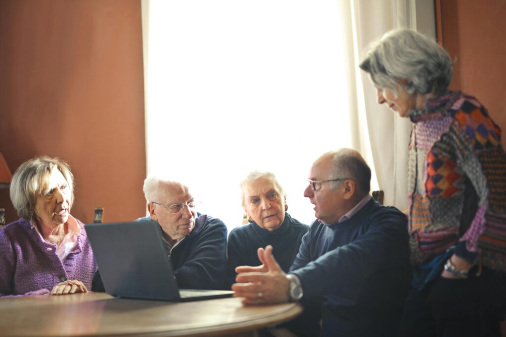 A group of older adults sits around a table having a serious discussion with a laptop open, reviewing California insurance plans and Medicare options together.