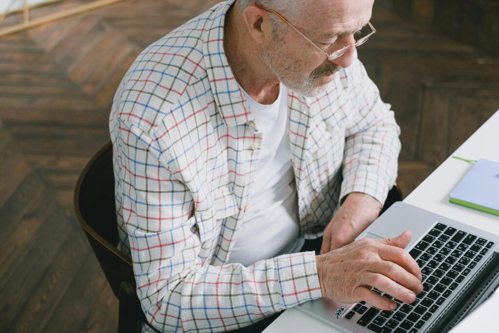 An elderly man types on a laptop at home, researching California insurance plans that work in tandem with his Medicare policy.